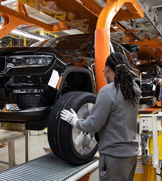 Automotive assembly line worker mounting wheel on SUV