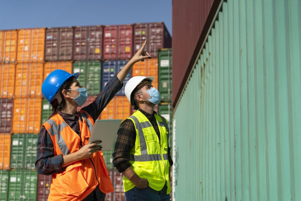 logistic engineer workers in hard hats pointing upwards to shipping crates