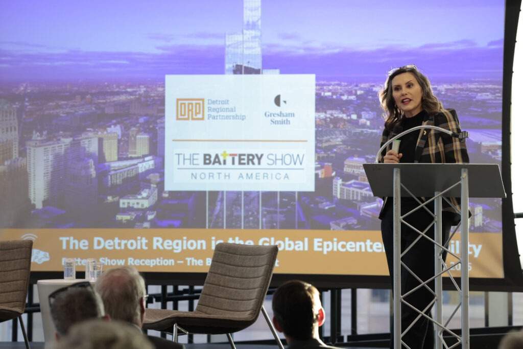 A woman holding a plaid jacket holding a microphone on stage.