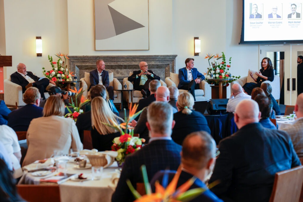 Panel of five people on stage talking, a crowd listens in