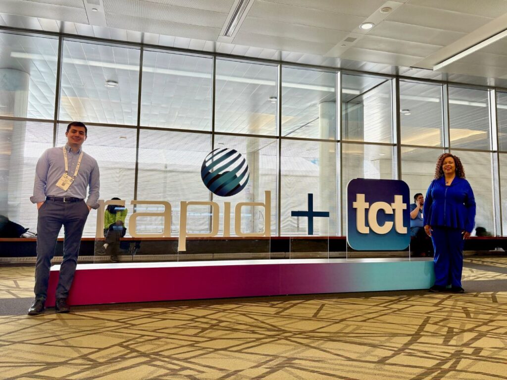 Two people standing next to a large conference sign