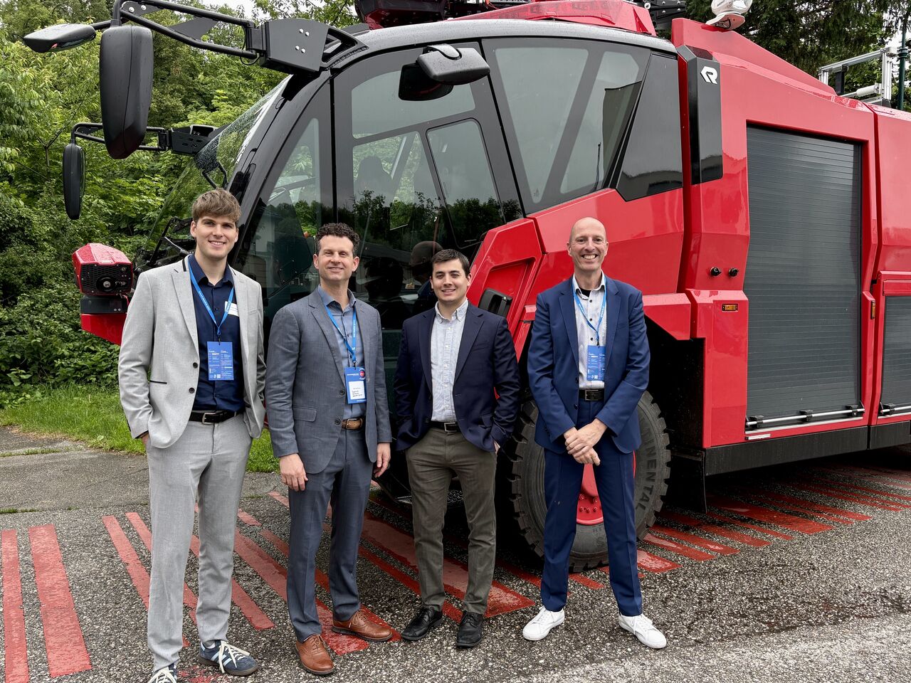 Four people standing side by side in front of a red vehicle